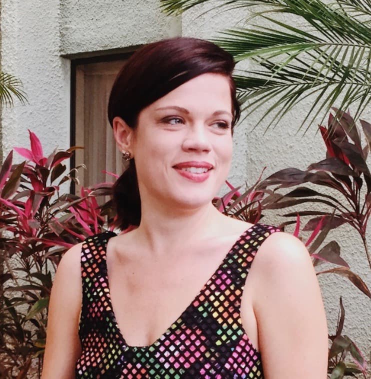 Smiling woman standing near plants outside.