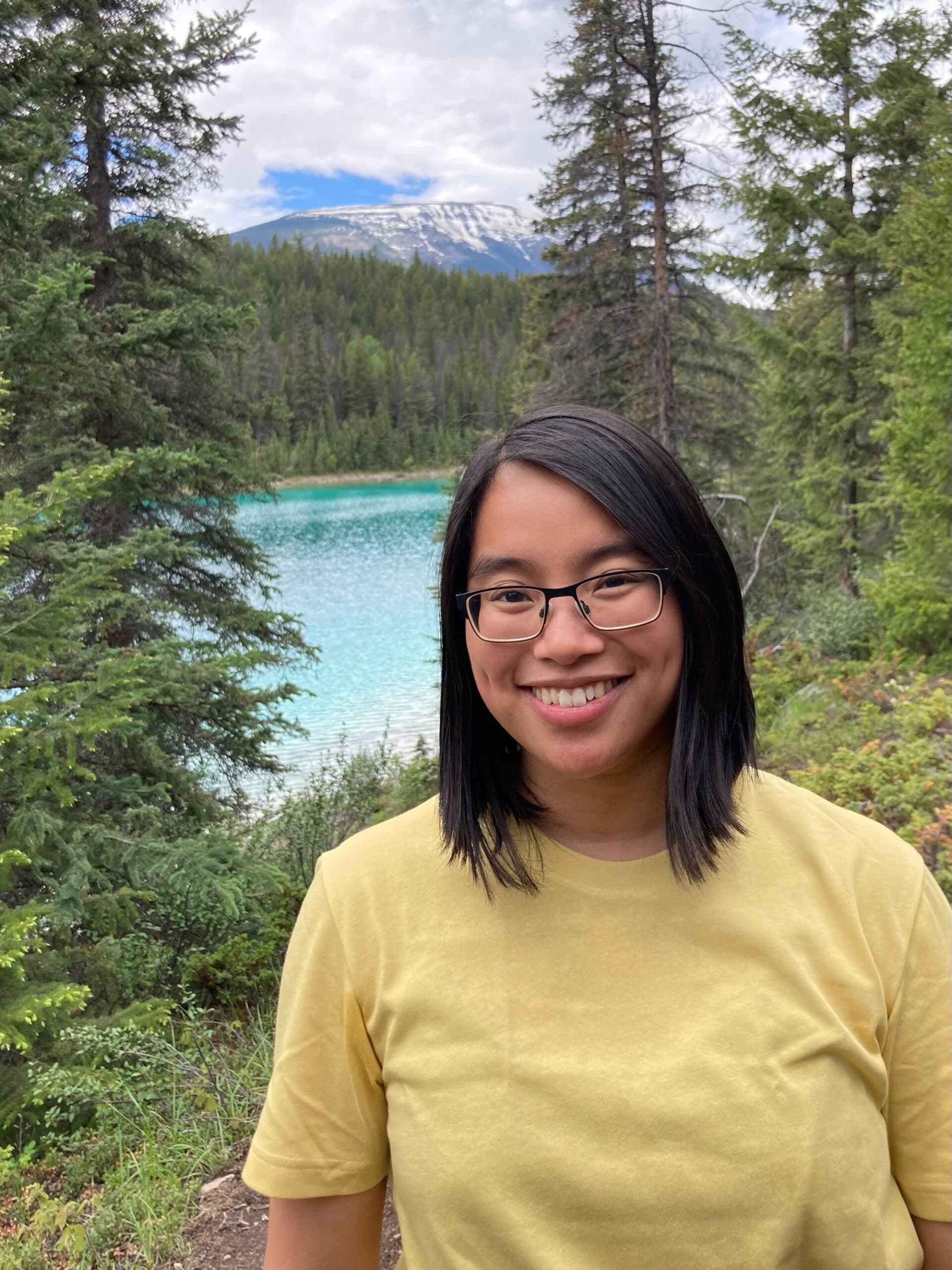 Person smiling by turquoise lake and forest