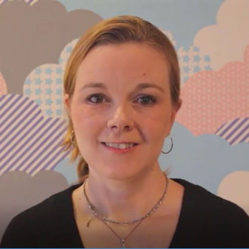 Smiling woman in front of colorful cloud wallpaper.