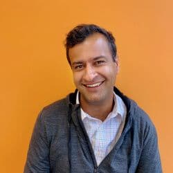 Smiling person against orange background in casual attire.