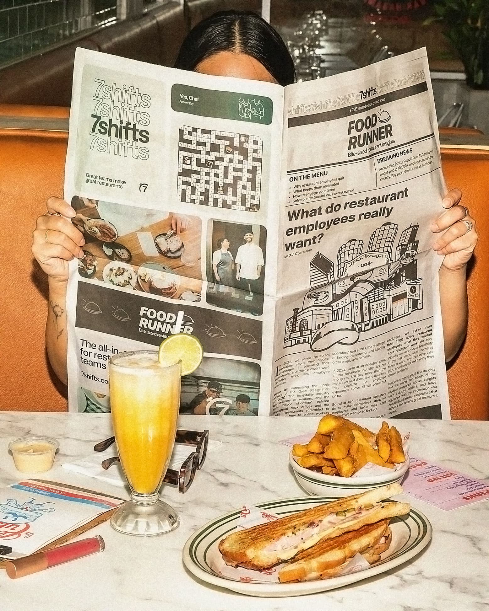 Person reads newspaper with breakfast at diner table.