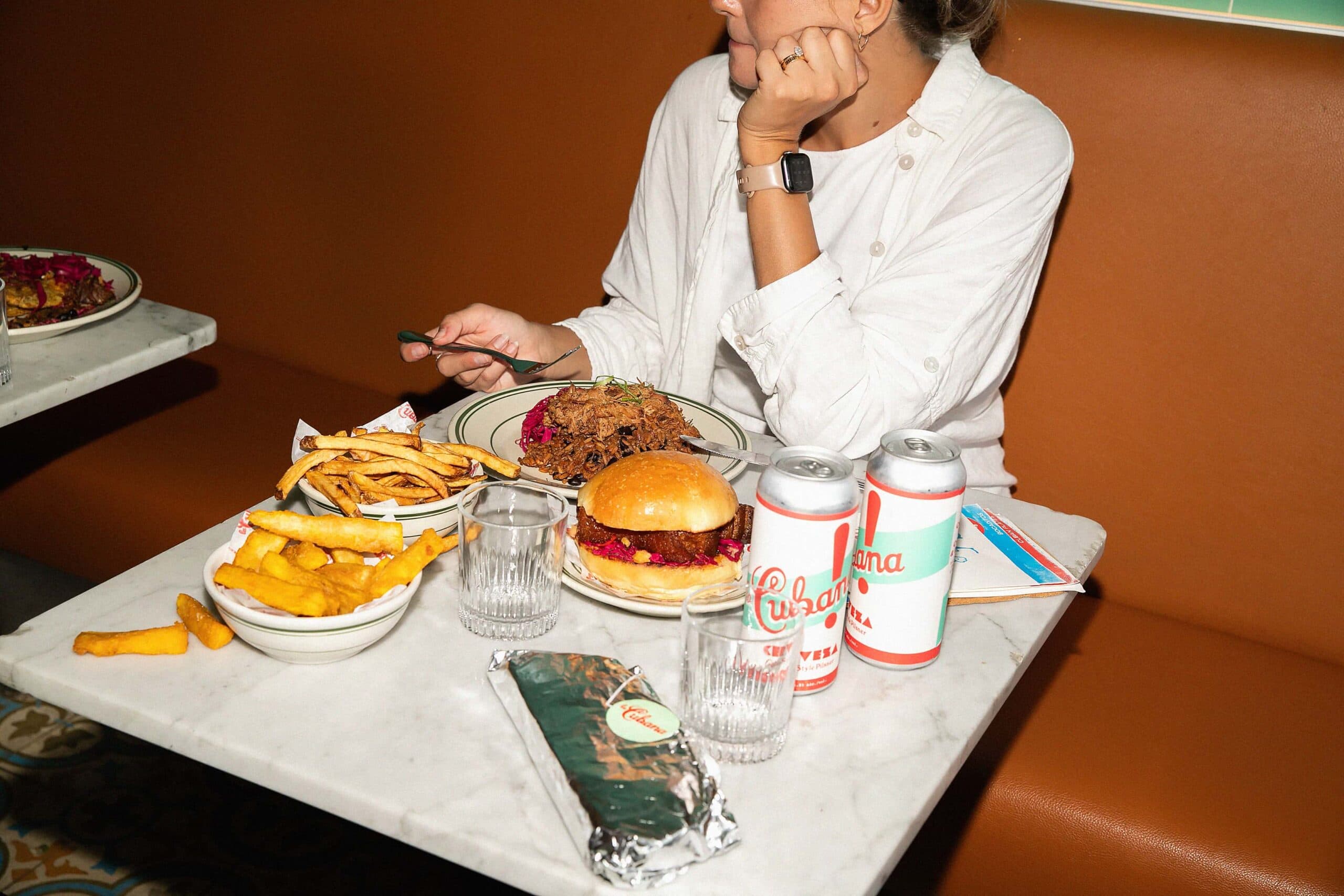 Person dining with fries, burger, and drinks.