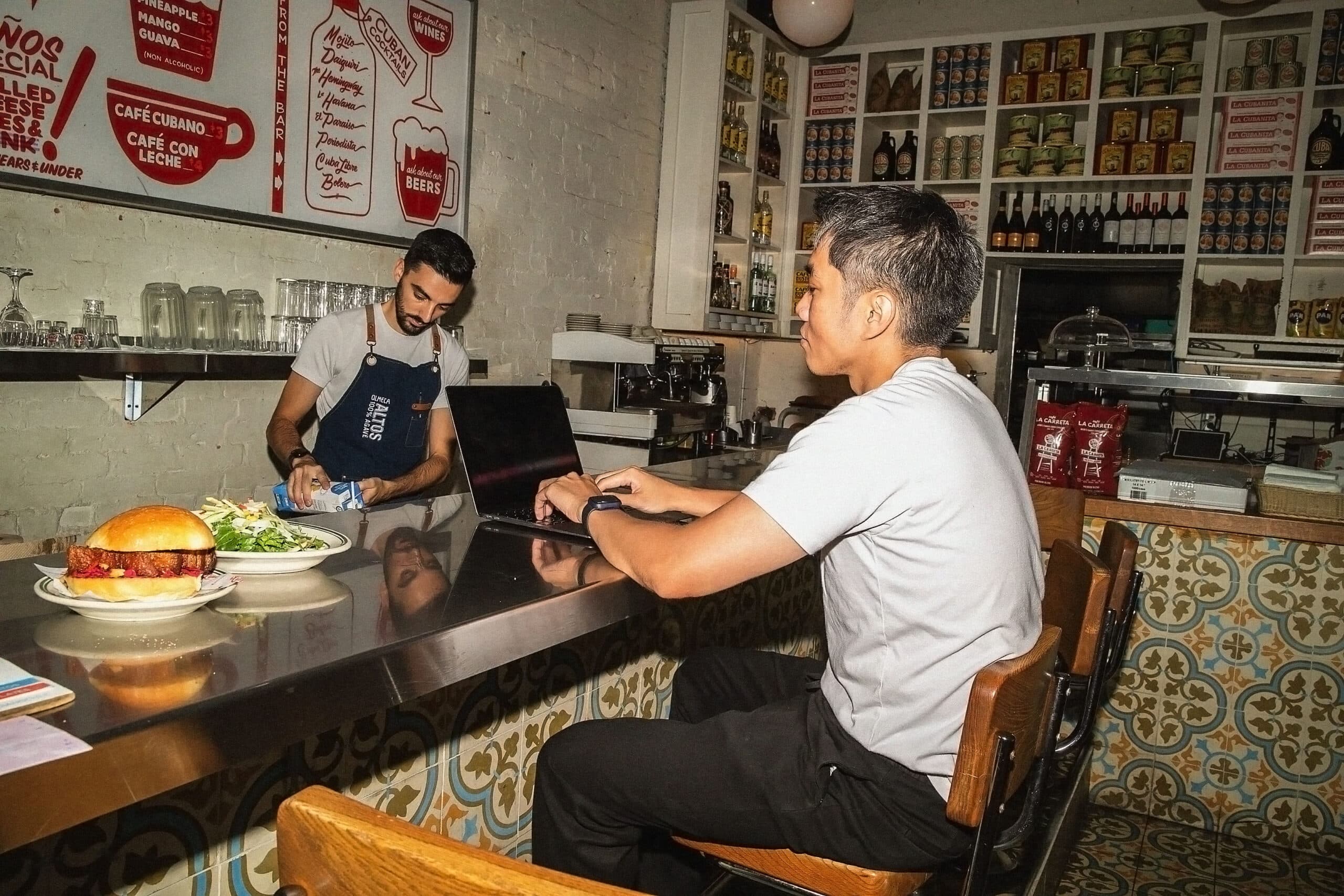 People in cafe working on laptop near counter.