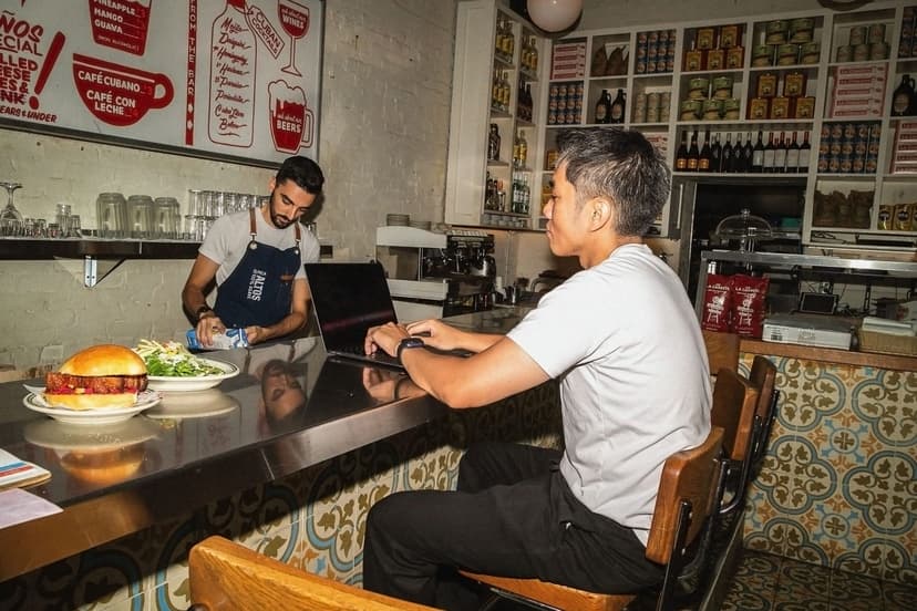 People in cafe working on laptop near counter.