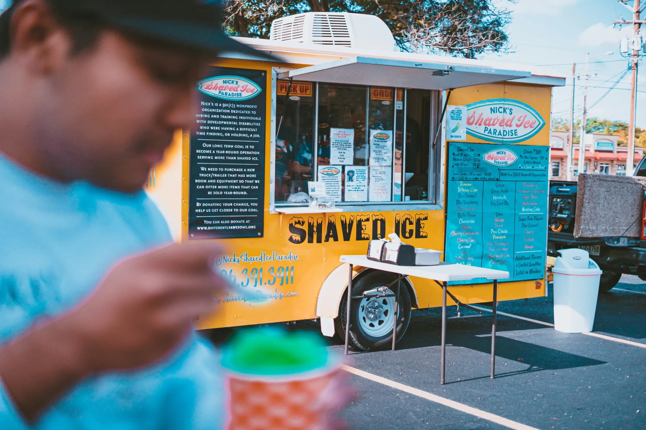 Yellow shaved ice truck with customer in foreground.