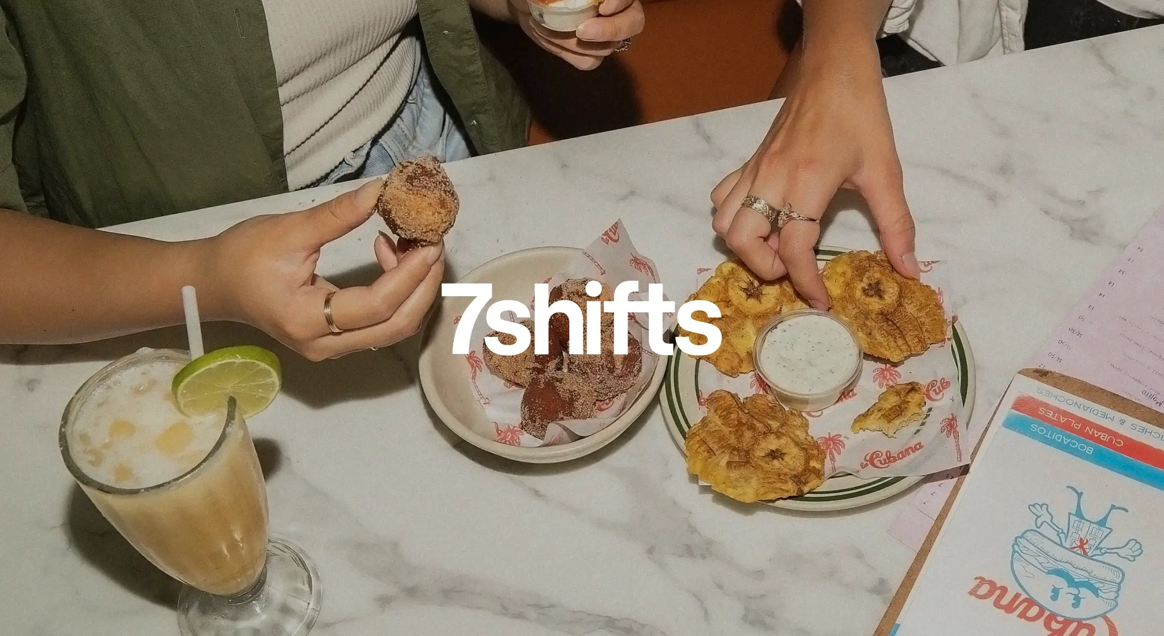 Hands eating appetizers with drink and menu