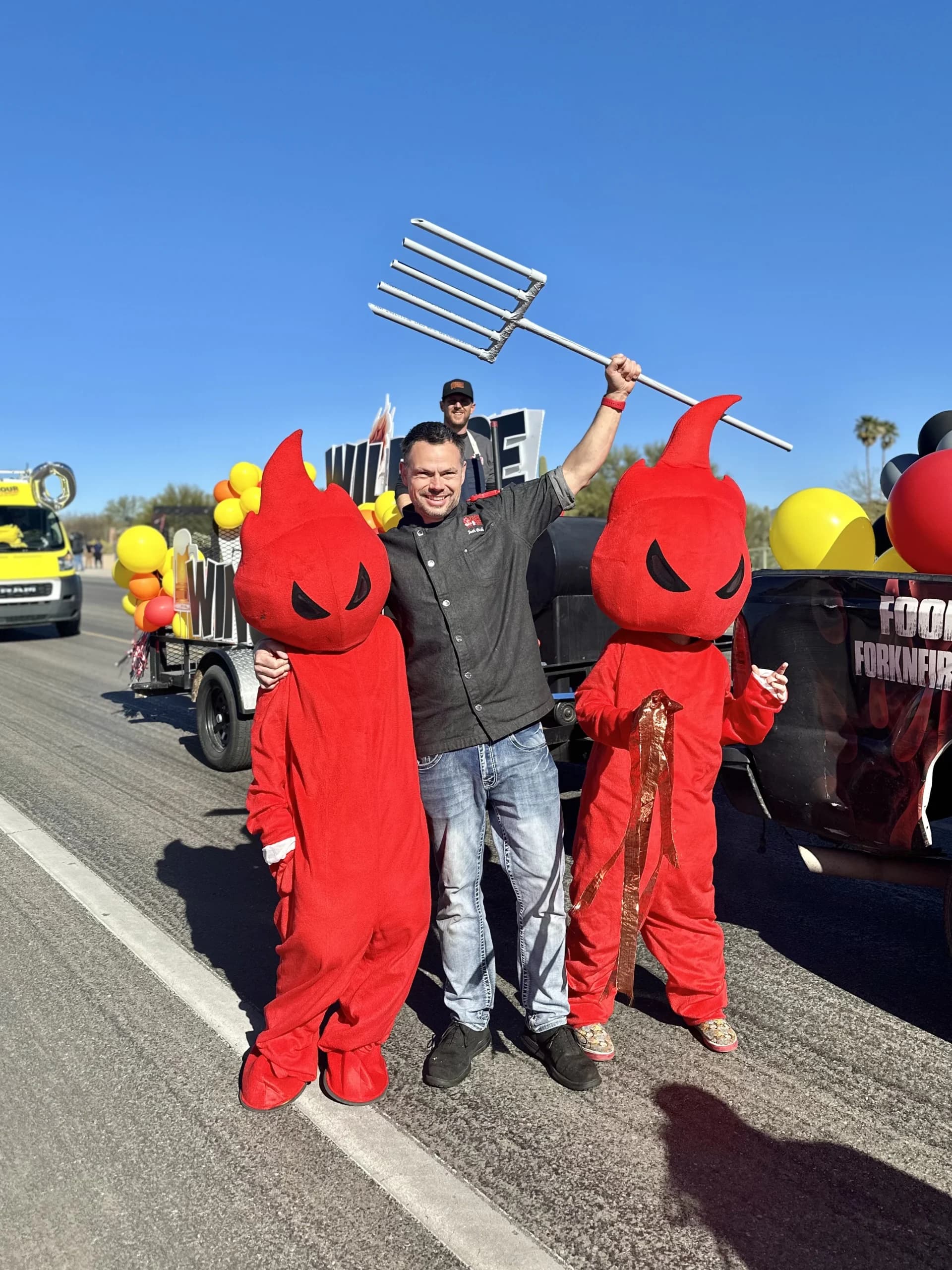 Man and red mascots at outdoor festival parade.