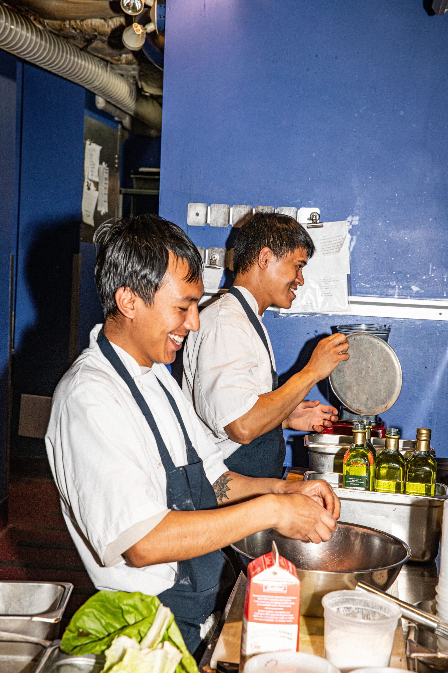 2 chefs prepping food in a restaurant kitchen against a blue wall