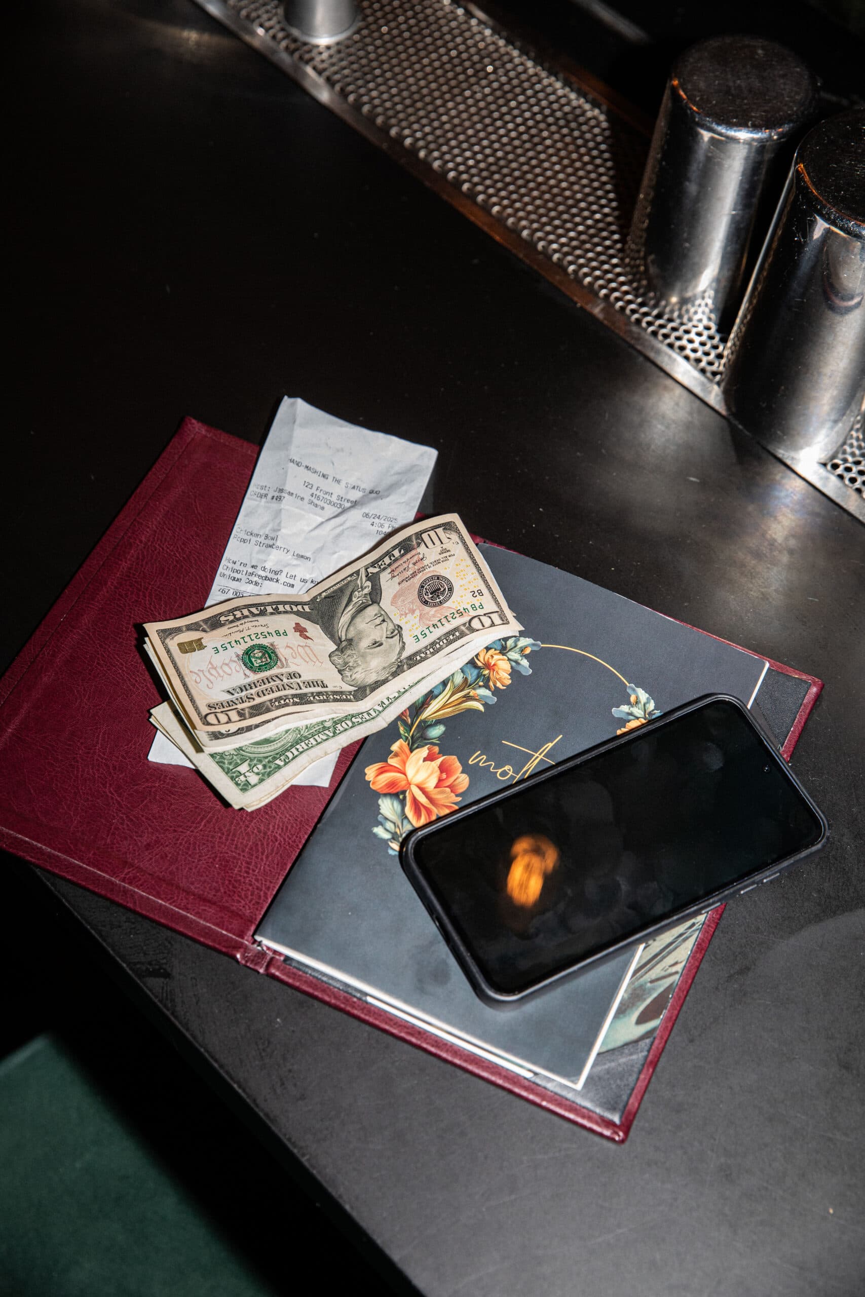 A phone, cash, and a receipt on top of a menu on a bar counter.