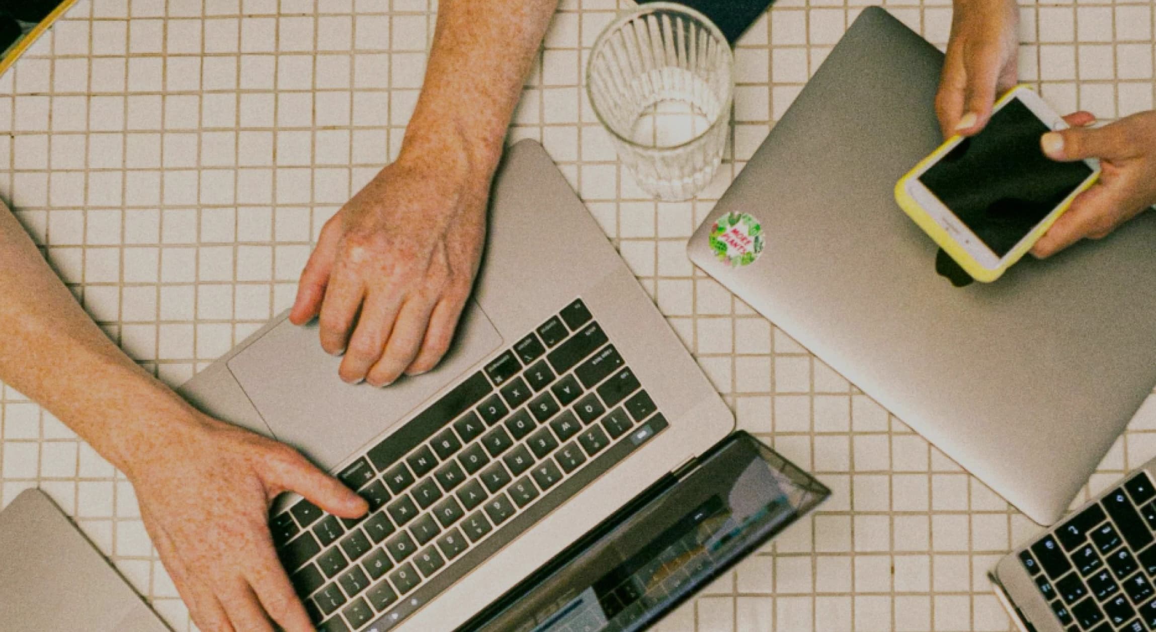 Person typing on laptop and person scrolling on phone at dining table