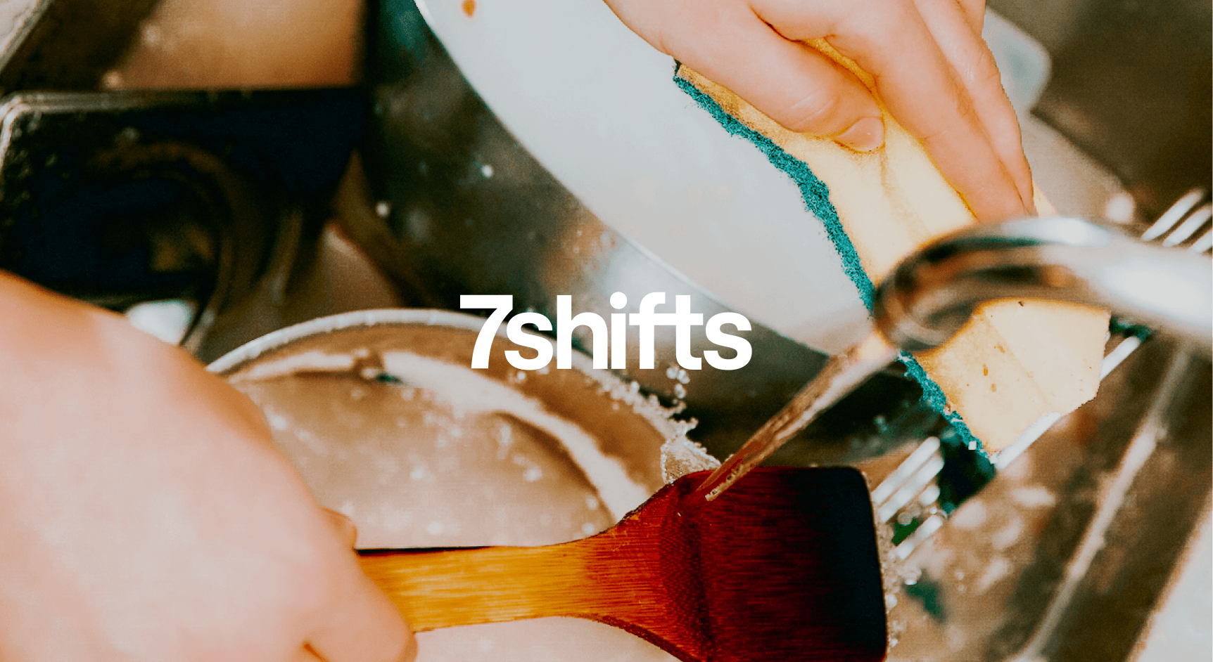 Person washing spatula in sink full of dishes