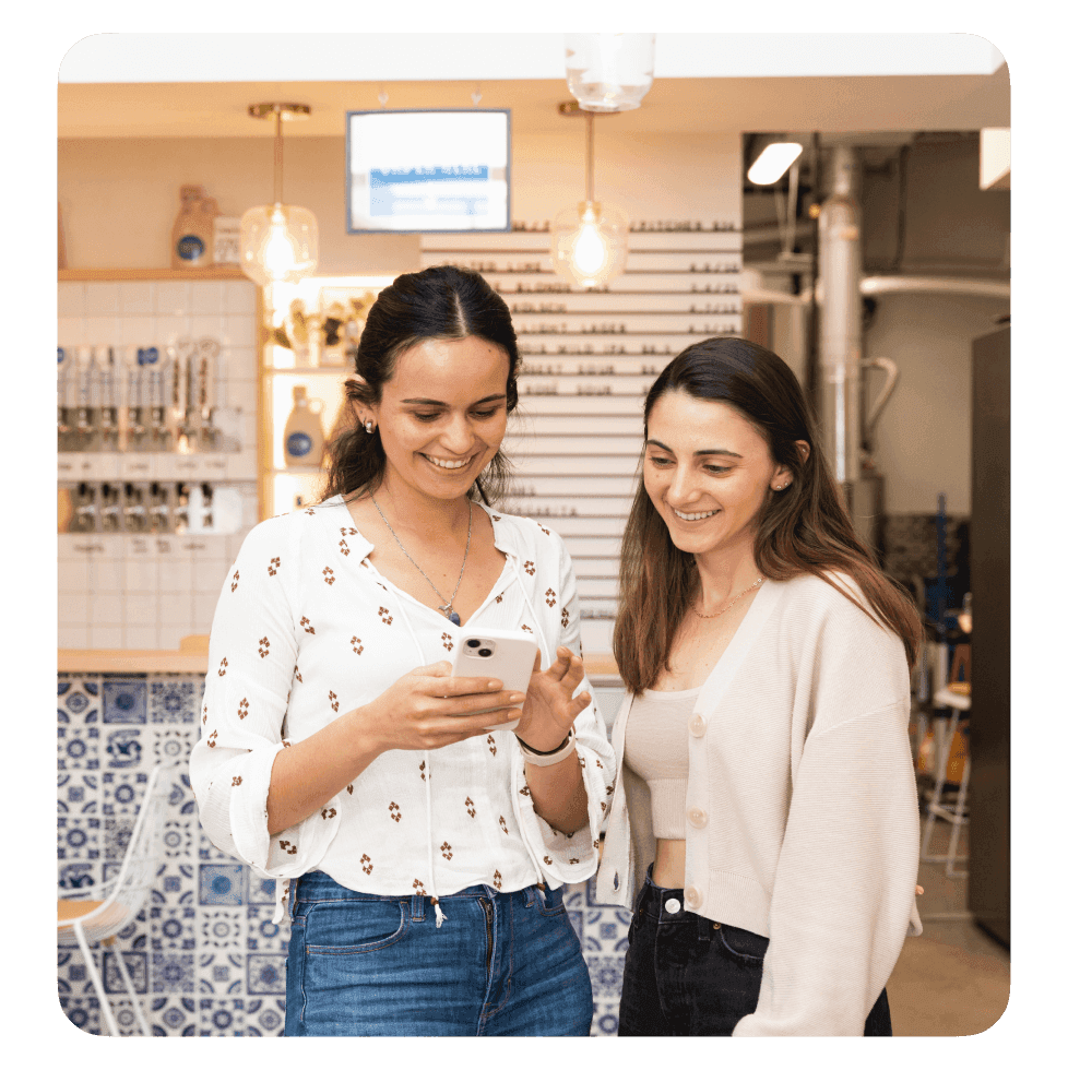 Two smiling female brewery employees looking at mobile device.