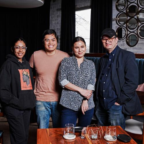 Event: March 15, 11am CST. Four people posing for a photo inside a restaurant