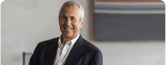 Founder and CEO of USHG, Danny Meyer wearing a suit and leaning on desk.