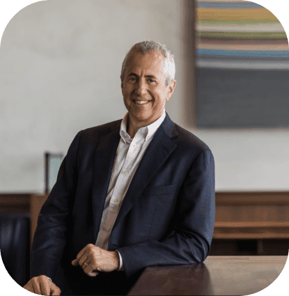 Founder and CEO of USHG, Danny Meyer wearing a suit and leaning on desk.